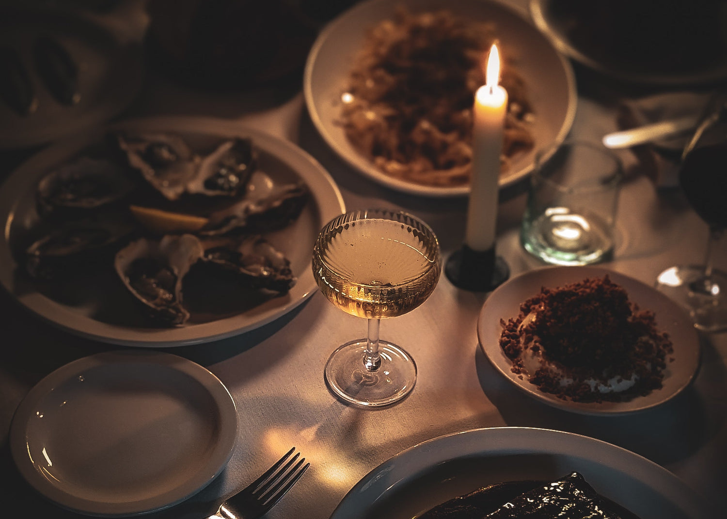 Dining table setting with plates, glasses, and a lit candle in a dimly lit room.