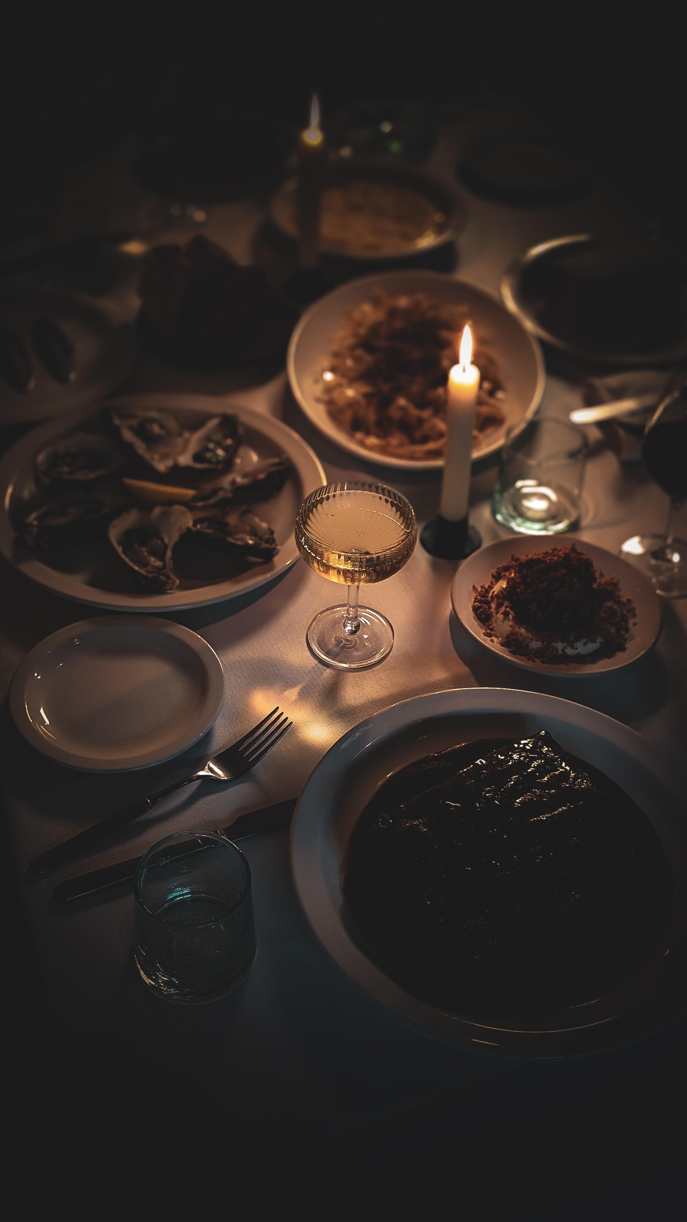 Dining table setting with plates, glasses, and a lit candle in a dimly lit room.