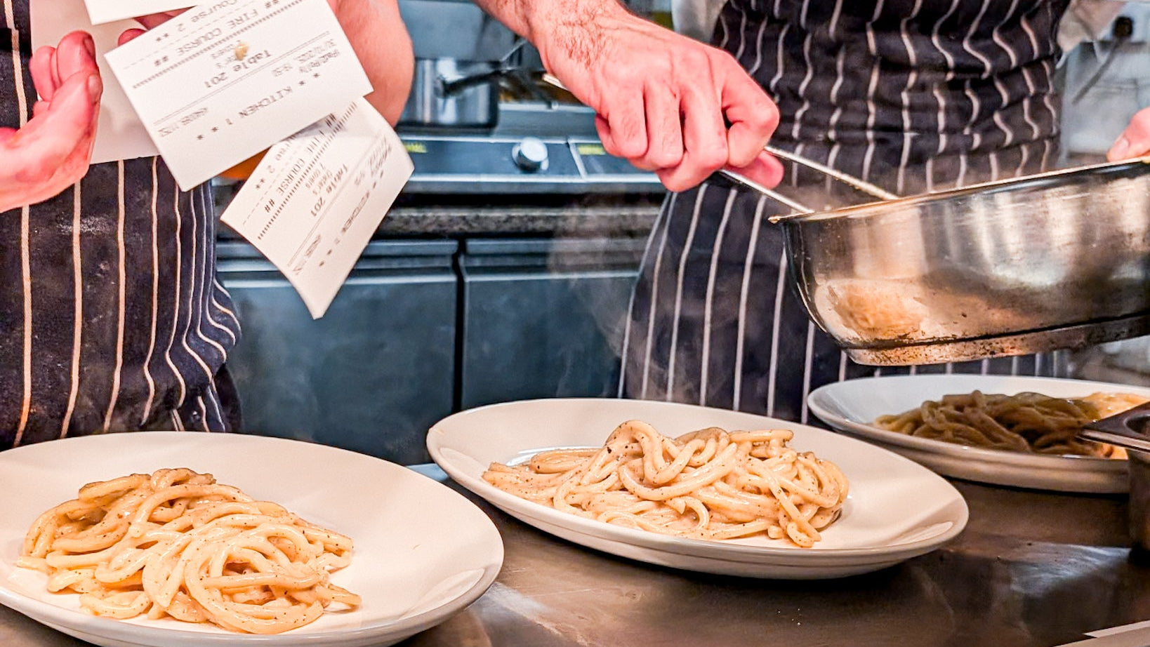 Culinary scene with pasta dishes on a counter, kitchen staff in the background.